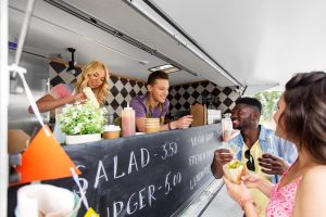 Young woman and man serving customers food from a catering van at a festival