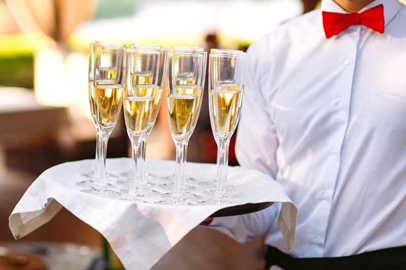 Waiter with red bowtie holding a tray with 6 champagne glasses on