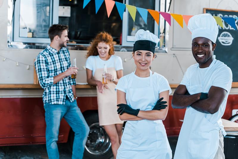 Two chefs with folded arms outside a mobile catering van at a festival