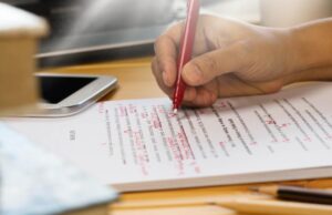 A close-up of a hand writing with a red pen on a CV, highlighting mistakes on it