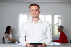 Sam Hickman standing in his office holding an iPad with two people working in the background