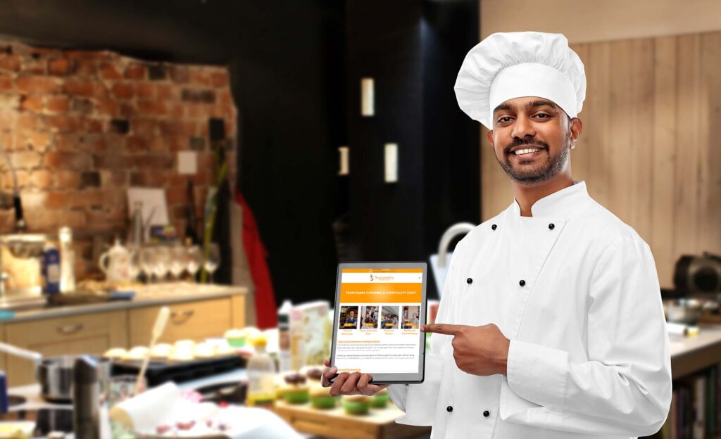 Male chef in a kitchen pointing at a tablet which is showing the Summerley Recruitment website's temporary staff page