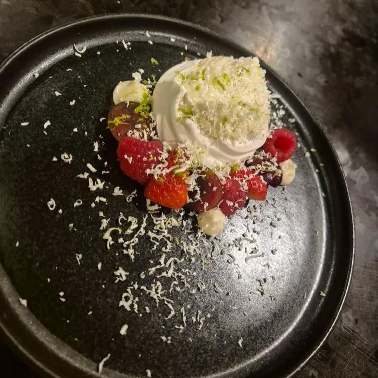 A black plate with a delicious looking dessert with berries, cream and meringue.